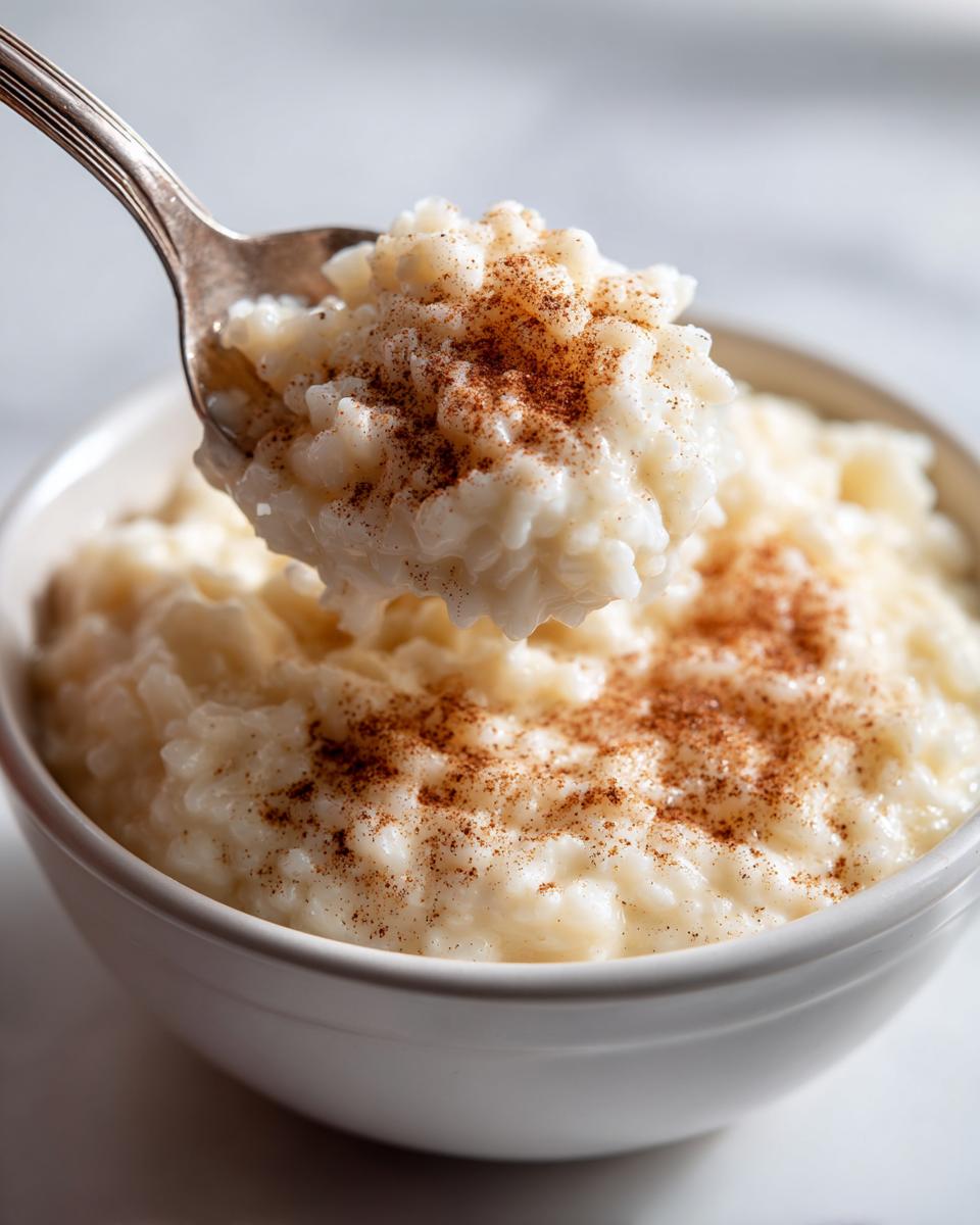 A spoonful of creamy rice pudding recipe topped with cinnamon being lifted from a white bowl.