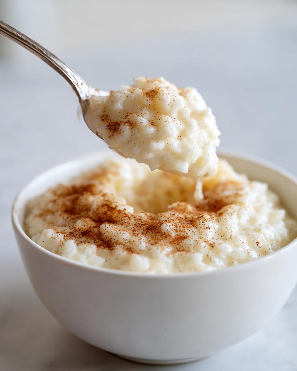 A spoonful of creamy rice pudding recipe topped with cinnamon being lifted from a white bowl.