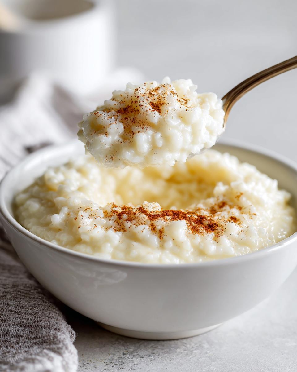 A spoonful of creamy rice pudding recipe topped with cinnamon being lifted from a white bowl.