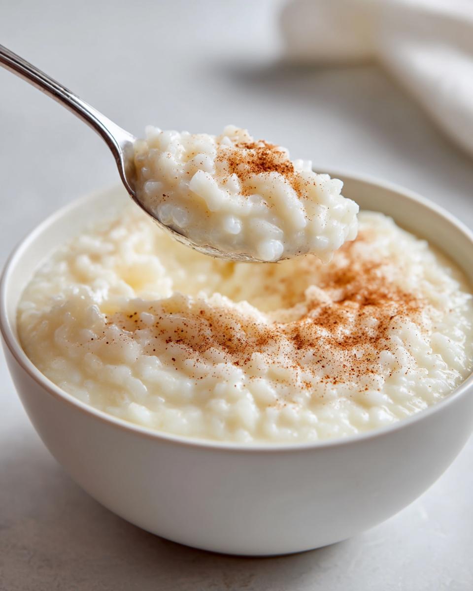 A spoonful of creamy rice pudding recipe topped with cinnamon being lifted from a white bowl.