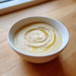 A close-up of creamy roasted cauliflower soup, swirled with olive oil and a sprinkle of pepper.