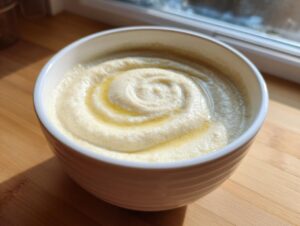 A close-up of creamy roasted cauliflower soup in a white bowl, drizzled with olive oil in a swirl pattern.
