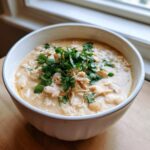 A close-up of a creamy white chicken chili, topped generously with fresh cilantro, served in a white bowl.