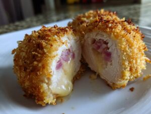 Close-up of a golden-brown, crispy chicken cordon bleu cut open to show melted cheese and ham filling.