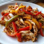Close-up of shredded chicken mixed with colorful bell pepper strips in a savory sauce, ready for crockpot chicken fajitas.