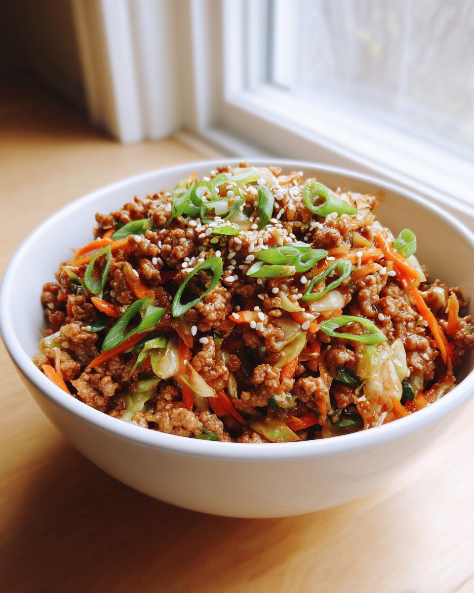 A white bowl filled with savory egg roll in a bowl mixture, topped with green onions and sesame seeds.