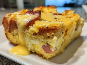 Close-up of a thick slice of eggs benedict casserole topped with melted cheese and drizzled hollandaise sauce.