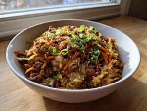 A close-up of a white bowl filled with savory egg roll in a bowl mixture, topped with green onions and sesame seeds.