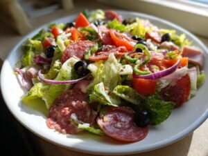 A vibrant close-up of a fresh grinder salad featuring salami, ham, lettuce, tomatoes, olives, and red onion.