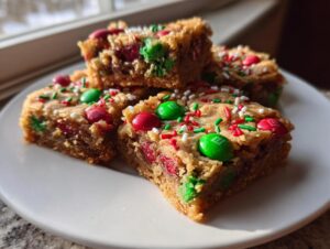 Close-up of four rich Christmas cookie bars topped with red and green M&Ms and festive sprinkles.