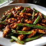 Close-up of glossy, saucy chicken and green beans skillet dish served in a white bowl.