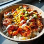 A close-up, brightly lit photo of a delicious shrimp bowl featuring seasoned shrimp over rice, topped with corn salsa, avocado, and a creamy white sauce.