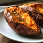 Close-up of a perfectly baked sweet potato, split open to show fluffy orange flesh seasoned with pepper.