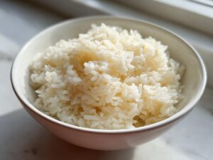 A close-up of a white bowl filled with fluffy, perfectly cooked butter rice, highlighted by natural sunlight.