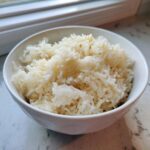 A close-up of fluffy, perfectly cooked butter rice served in a white bowl near a window.