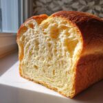 Close-up cross-section of a rich, golden condensed milk bread loaf showing its soft, airy crumb texture.