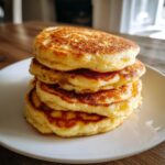 A tall stack of four golden brown, fluffy sourdough discard pancakes on a white plate.