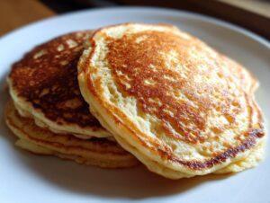 Close-up of a stack of three fluffy sourdough discard pancakes with golden brown, bubbly tops served on a white plate.