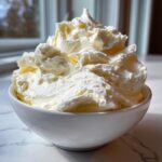 A large swirl of light, fluffy vanilla buttercream frosting piled high in a small white bowl.