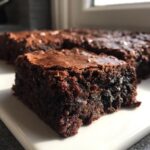 Close-up of a rich, fudgy slice of Oreo brownies with a shiny top crust, sitting on a white plate.