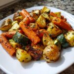A close-up of perfectly cooked Garlic Herb Roasted Veggies including carrots, potatoes, and zucchini on a white plate.
