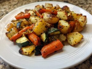 A close-up of perfectly roasted potatoes, carrots, and zucchini seasoned with herbs, showcasing the results of the Garlic Herb Roasted Veggies recipe.