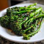 Close-up of bright green, slightly charred broccolini tossed in garlic and lemon sauce on a white plate.