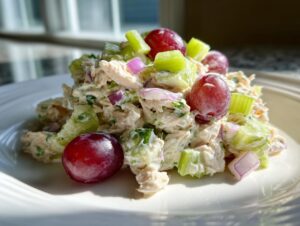 A mound of creamy greek yogurt chicken salad mixed with celery, red onion, and topped with whole red grapes.