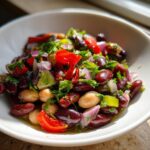 Close-up of a vibrant, colorful bean salad featuring kidney beans, chickpeas, red onion, red pepper, and fresh herbs.