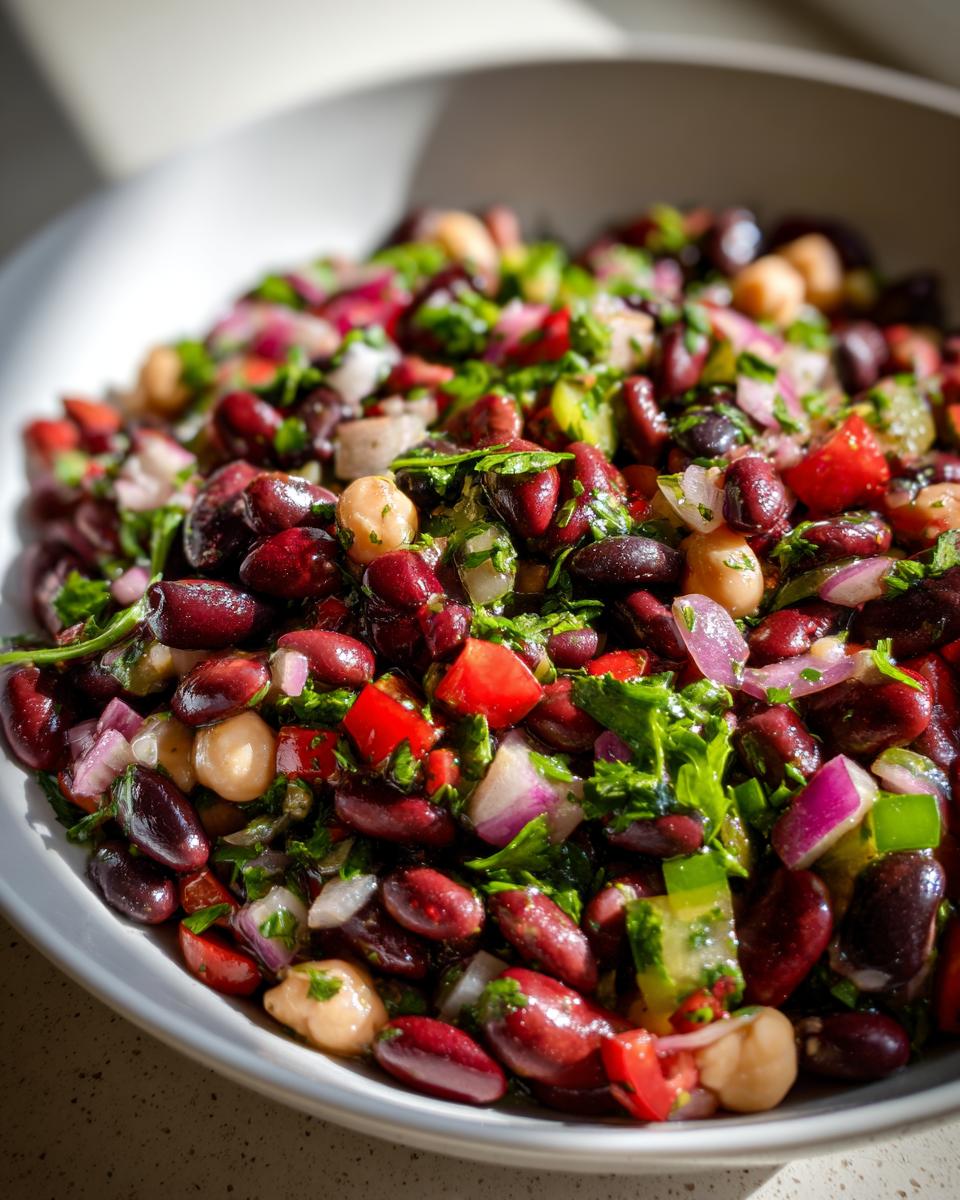 Close-up of a vibrant, fresh bean salad featuring kidney beans, chickpeas, red onion, and herbs.