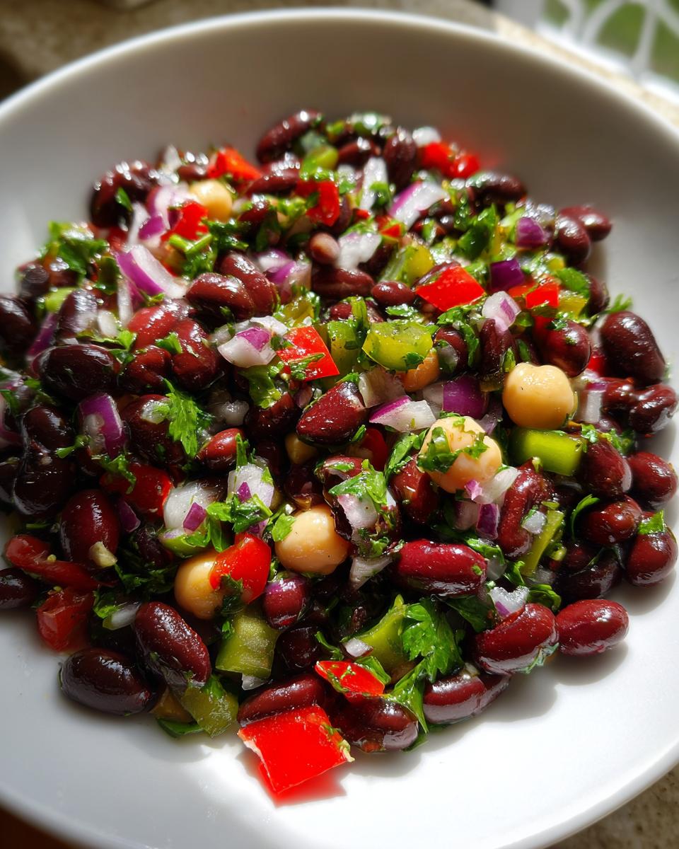 Close-up of a vibrant, colorful bean salad featuring black beans, chickpeas, red onion, red pepper, and parsley.