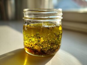 A glass jar filled with homemade salad dressing featuring olive oil, fresh herbs, and garlic pieces.