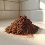 A mound of rich brown homemade hot cocoa mix powder sitting on a light countertop with a tiled backsplash.