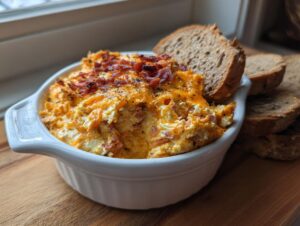 A close-up of hot reuben dip topped with melted cheese and bacon bits, served with slices of rye bread.