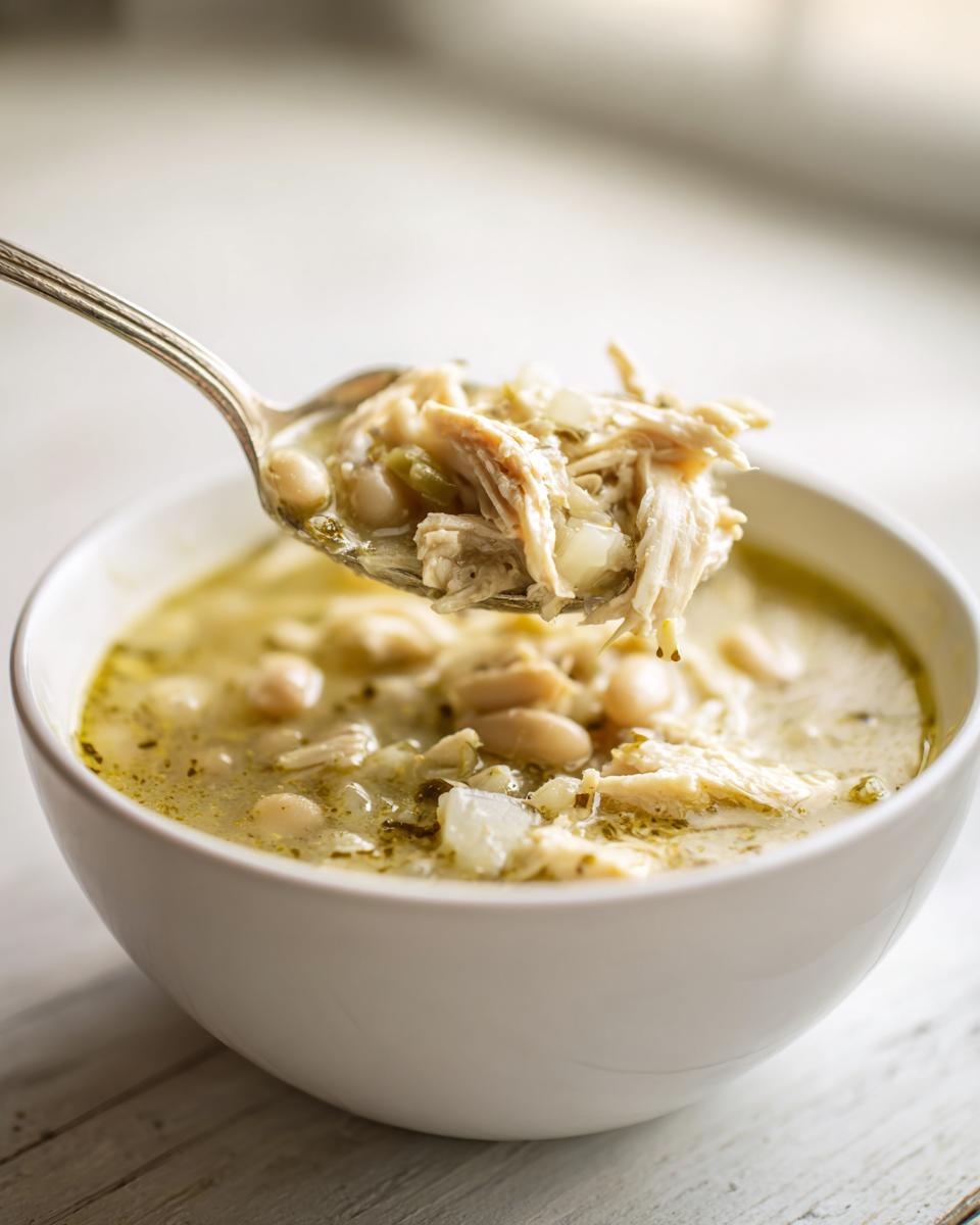 A spoonful of shredded chicken and white beans lifted from a bowl of creamy instant pot white chicken chili.