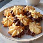 A plate piled high with star-shaped Italian butter cookies dipped in dark chocolate and sprinkled with nuts.