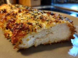 Close-up of a juicy baked ranch chicken breast, showing the white interior and golden, herbed topping.