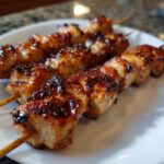 Close-up of three skewers loaded with juicy, caramelized chicken skewers, glistening with a dark glaze.