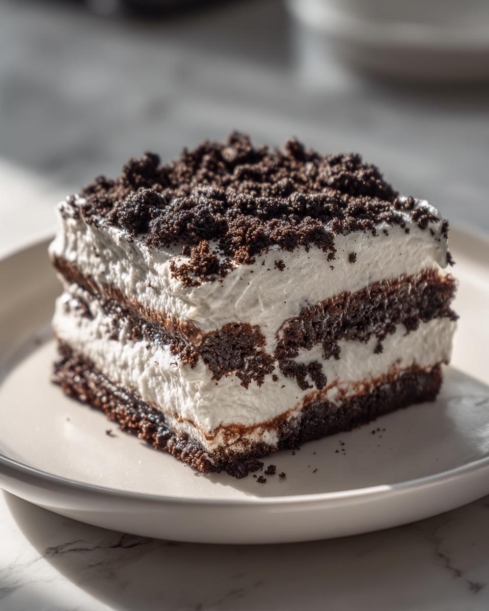 Close-up of a square slice of layered dirt cake featuring dark chocolate cookie crumbs and thick white cream filling.