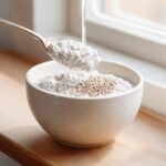 A spoonful of creamy coconut chia pudding is lifted from a bowl while more liquid is poured in, showing the texture.