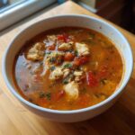 Close-up of a white bowl filled with rich, tomato-based Maryland crab soup, featuring visible chunks of white crab meat and parsley.