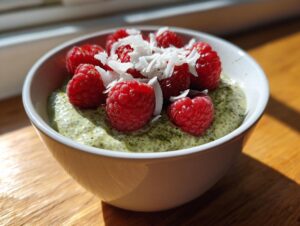 A close-up of creamy matcha chia pudding topped with fresh raspberries and shredded coconut.