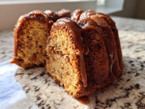 Close-up of a moist apple bundt cake slice topped with rich caramel glaze dripping down the sides.