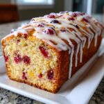 A close-up of a freshly baked loaf of moist cranberry orange bread topped with a thick white citrus glaze.