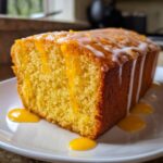 A moist slice of orange juice cake topped with white glaze and dripping orange syrup.