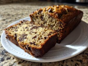 A close-up of moist vegan banana bread with chocolate chips, sliced on a white plate.