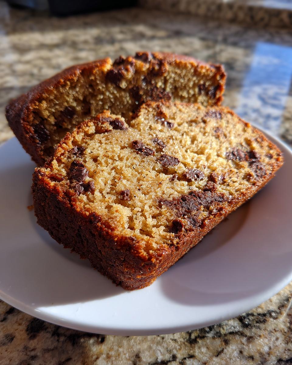 Two thick slices of moist vegan banana bread studded with chocolate chips, resting on a white plate.
