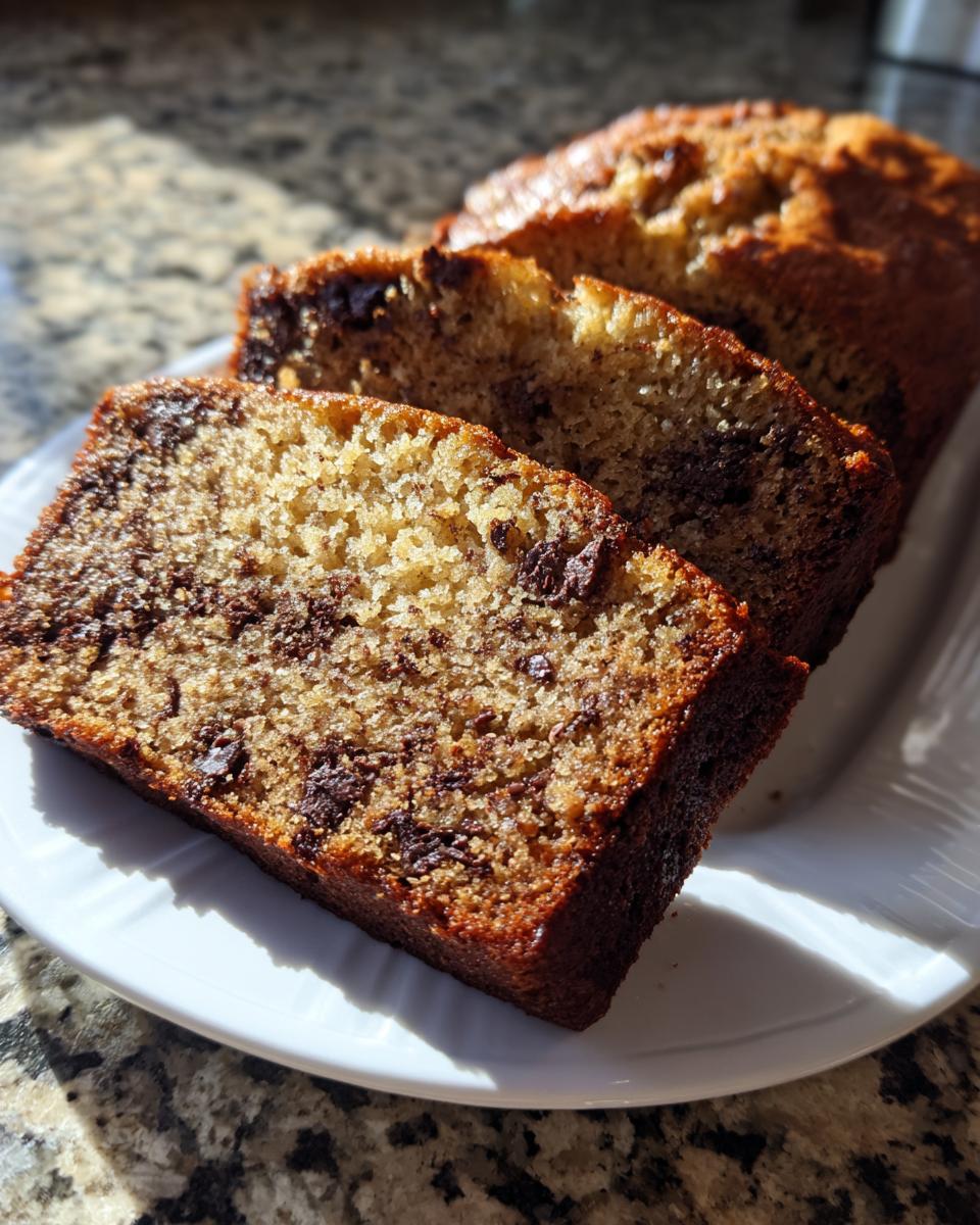 Close-up of three moist slices of vegan banana bread loaded with chocolate chips, resting on a white plate.