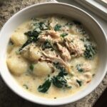 A close-up of a white bowl filled with creamy Olive Garden Chicken Gnocchi Soup, featuring shredded chicken, potato gnocchi, and wilted spinach.