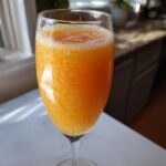 Close-up of a bright orange, fizzy bellini recipe served in a champagne flute glass.